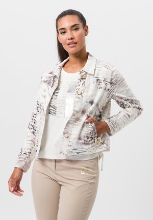 Veste en denim à manches courtes, à motifs, avec une base pâle et des designs abstraits marron. Dotée de boutons dorés et d'une poche latérale.