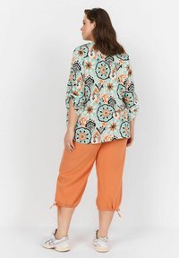 Blommönstrad, lös passform topp i mintgrön med orange och svarta accenter; matchad med klara orangea cropped-byxor med dragsko vid ärmsluten.