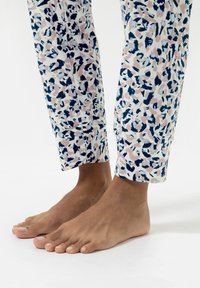 Pantalon de pyjama à motifs rose, marine et blanc, avec un design abstrait, coupe droite et ourlet revers. Pieds nus visibles.