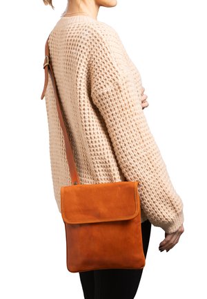 Borsa a tracolla in pelle di un ricco marrone con chiusura a pattina, texture liscia e tracolla regolabile, indossata sopra un maglione beige di lana.