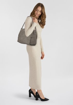 Abito beige a maniche lunghe realizzato in un materiale morbido, abbinato a una borsa grigia con trama e scarpe con tacco nero, in piedi su uno sfondo bianco.