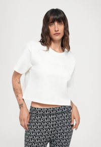 White cropped t-shirt with embroidered "MICHAEL KORS" logo; paired with dark gray leggings featuring a repeating monogram pattern.