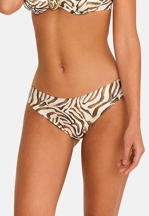 Femme portant un bas de bikini beige et marron à imprimé zèbre et un haut assorti avec un détail d’anneau doré, montrée du creux de l’abdomen jusqu’aux cuisses.
