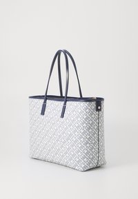 Borsa tote in tessuto bianco texturizzato con un motivo geometrico blu. Manici e bordo superiore in blu navy, con dettagli in zip dorati.