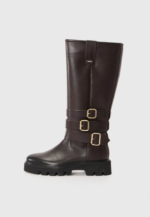 Brown leather knee-high boots with three decorative buckles, a textured finish, and a rugged black sole. Sleek, fitted design with minimal accents.