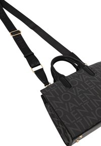 Borsa nera con motivo a logo in rilievo, doppi manici e una tracolla removibile. Presenta dettagli dorati e materiale texturizzato.