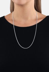 Silverkedja med en slät, texturerad yta som hänger ner från en svart ribbad topp, med en enkel, avlång design.