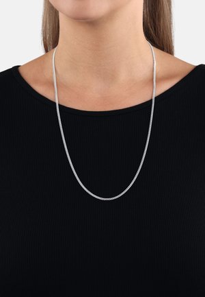 Collar de cadena de plata con una superficie lisa y texturada, que cae desde una blusa negra con ribetes, presentando un diseño simple y alargado.