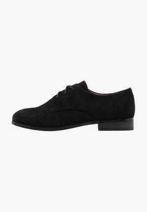 Chaussure à lacets en suede noir avec un bout arrondi, des détails de couture subtils et un talon bas et plat. Texture lisse avec un design minimaliste.