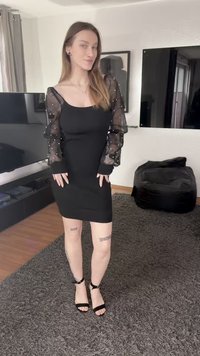 Μαύρο φόρεμα με εφαρμοστή γραμμή και διαφανείς φουσκωτές μανσέτες διακοσμημένες με λευκά μαργαριτάρια· φορεμένο με μαύρα τακούνια με λουράκι στον αστράγαλο και ορατά τατουάζ στα πόδια.