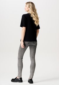 Svart t-shirt med kort ärm, kombinerad med grå slim fit-jeans och kraftiga svarta skor, som visar en smidig tygkvalitet och en minimalistisk design.