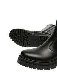 Stivali alla caviglia neri in pelle con una suola in gomma spessa e con texture. Chiusura con cerniera laterale e dettagli a cucitura caratterizzano il design elegante.