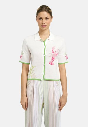 Woman wearing a white short-sleeve buttoned shirt with green trim and pink sea creature designs, paired with high-waisted striped pants.