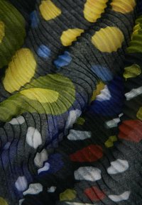 Durchsichtiger schwarzer Stoff mit bunten Punkten in Gelb, Blau, Weiß und Rot, der eine strukturierte, zerknitterte Optik aufweist.