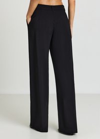 Schwarze Hose mit weitem Bein und glatter Textur, die kleine Perforationen im Stoff aufweist. Ausgestattet mit Taschen und einem taillierten Bund.