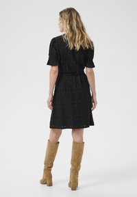 Rochie neagră din dantelă florală cu mâneci scurte tip puff, talie strâmtă și tiv până la genunchi, asortată cu cizme bej din velur până la genunchi.