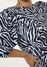 Zebra-patterned top with puffed sleeves, featuring a light blue and black color scheme. Textured fabric with a relaxed fit.