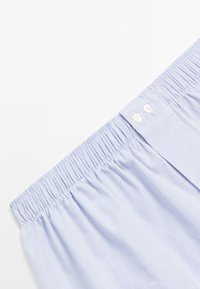 Light blue striped cotton shorts with an elastic waistband and two white button details at the front. Soft, textured fabric.