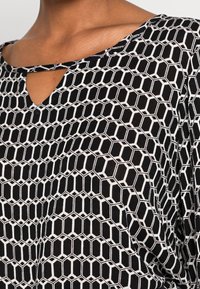 Haut noir et blanc avec un motif géométrique en nid d'abeille, doté d'un col en trou de serrure et d'un tissu léger.