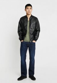 Giubbotto bomber in pelle nera con colletto rotondo, chiusura con zip e polsini a coste. Abbinato a una t-shirt verde scuro e jeans blu.