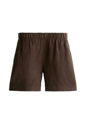 Ruka v vrecku, nosiac vysoké, voľné tmavohnedé šortky s elastickým pásom a zahnutým lemom, v kombinácii s pruhovaným topom.