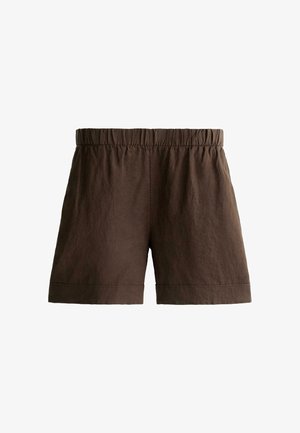 Hånd i lommen iført højtaljede, løstsiddende mørkebrune shorts med elastisk taljebånd og opbukket kant, kombineret med en stribet top.