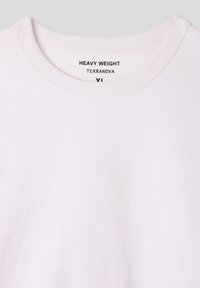 Biała, ciężka koszulka z okrągłym dekoltem. Posiada gładką, matową teksturę oraz nadrukowaną metkę: "HEAVY WEIGHT TERRANOVA" pod kołnierzykiem.