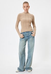 Maglione a coste beige con scollatura rotonda, abbinato a jeans a gamba larga di un blu chiaro. Tessuto liscio con motivo a righe verticali.
