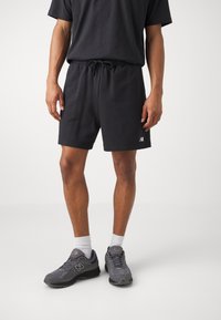 Black cotton shorts with an elastic drawstring waist, paired with gray sneakers featuring a prominent logo and white ankle socks.