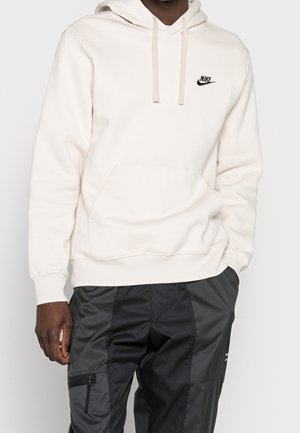 Light beige hoodie made from soft fabric, featuring a kangaroo pocket and branded black Nike logo on the chest. Adjustable drawstring hood.