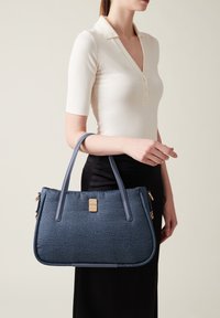 Borsa blu testurizzata con manici lisci, accessori in oro e una silhouette strutturata. Si abbina a un top aderente e una gonna.