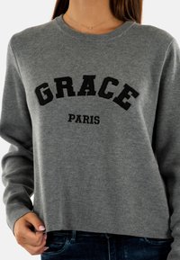 Felpa grigia con collo tondo, caratterizzata da testo ricamato in nero "GRACE" e "PARIS". Tessuto morbido e vestibilità comoda. Maniche lunghe.