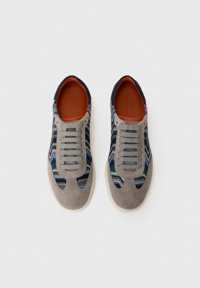 Hallid gray sneaks mitmevärviliste sakilise kangaga külgedelt ja hallide paeltega, vaadatuna ülevalt valgel taustal.