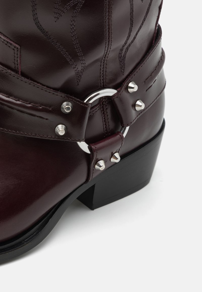 Bordowe skórzane kowbojskie buty z wyszywanymi wzorami, srebrnymi akcentami oraz grubym czarnym obcasem.