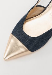 Chaussure en denim et métallisée dorée à bout pointu avec un design découpé, présentant un embout lisse doré et un dessus en denim texturé.