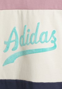 Adidas Sweatshirt mit einem strukturierten türkisfarbenen Logo auf einem cremefarbenen Hintergrund, versehen mit horizontalen Streifen in Pink und Marineblau.