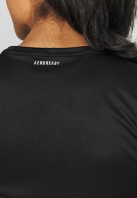 Svart träningsskjorta med en mjuk textur och rundad halsringning, med "AEROREADY" tryckt i vitt på baksidan.