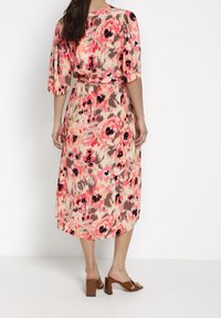 Robe midi fleurie en tissu doux avec des fleurs roses et beige, manches courtes, taille cintrée et ourlet tombant sous le genou.