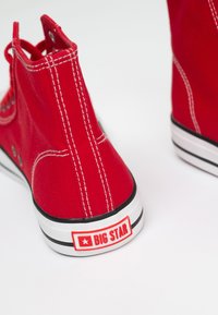 Czerwone płócienne sneakersy typu high-top z białym przeszyciem i gumową podeszwą, z białym i czerwonym logo "BIG STAR" na pięcie.