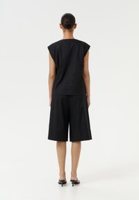 Črn laneni top z dolgimi, strukturiranimi rokavi, v kombinaciji s črnimi širokimi hlačami. Preprost dizajn in sproščen kroj, ki dopolnjuje minimalistični slog.