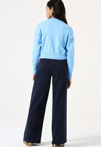 Hellblaues Strickpullover mit Rundhalsausschnitt, kombiniert mit dunkelblau gestreiften, weit geschnittenen Hosen. Das Outfit hat eine lockere Passform und gerippte Ärmelbündchen.
