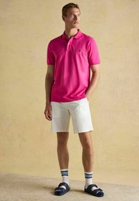 Roosa polo-särk, valged lühikesed püksid, tumesinised sandaalid ja triibulised sokid. Lühikesed varrukad, klassikaline krae ja väike logo rinnal.