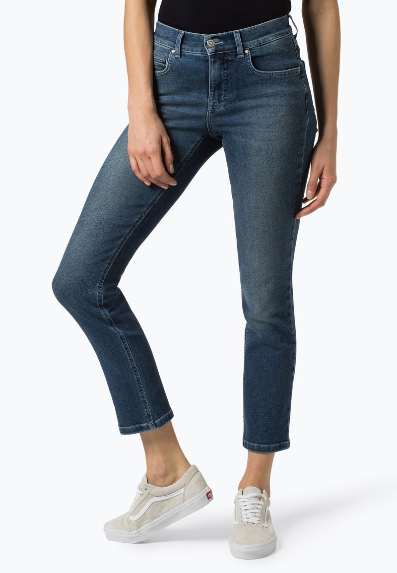Jeans in denim blu scuro con una vestibilità affusolata, vita media, cinque tasche e orlo sfilacciato. Abbinati a sneaker casual di colore chiaro.