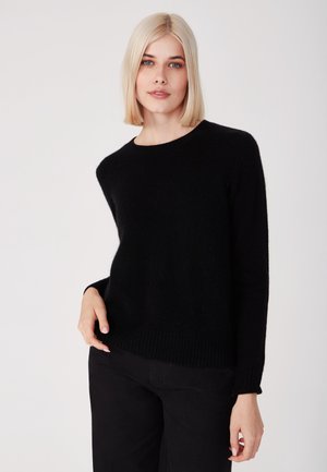 Zwarte gebreide trui met een ronde hals en lange mouwen, voorzien van ribgebreide randen en een zachte textuur. Draagt een zwarte broek.