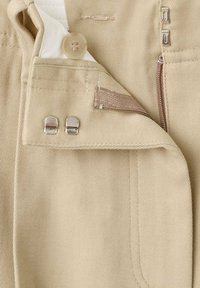 Beige broek met een knoop, rits en twee metalen sluitingen. Gerefineerde stof met zichtbare stiksels en een gladde voering aan de binnenkant.