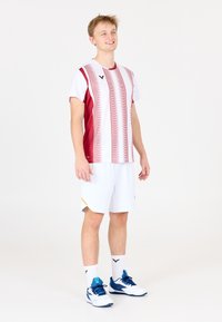 Rød og hvid stribet sports skjorte, parret med hvide shorts. Blå og hvide sportssko, med logoer på tøj og sokker.