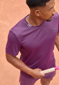 T-shirt de sport violet à manches courtes, avec un accent rayé sur le col. Le tissu est léger, adapté aux activités sportives.