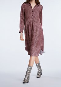 Robe à manches longues avec boutons, de couleur bordeaux, ornée de petits motifs floraux, taille cintrée et jupe fluide. Associée à des bottes imprimé serpent montant jusqu'aux genoux.