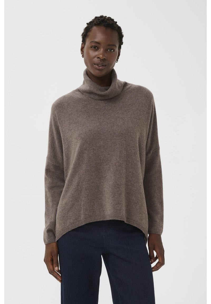 Suéter de punto marrón con un alto cuello vuelto, ajuste relajado y hombros caídos. Tela texturizada con un acabado suave, combinado con jeans oscuros.