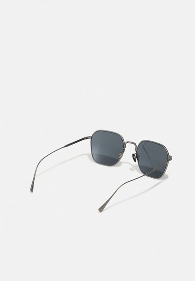 Ochelari de soare cu un cadru geometric, octagonal, de culoare gri închis, cu lentile închise și brațe subțiri din metal, având detalii subtile pe brațe.